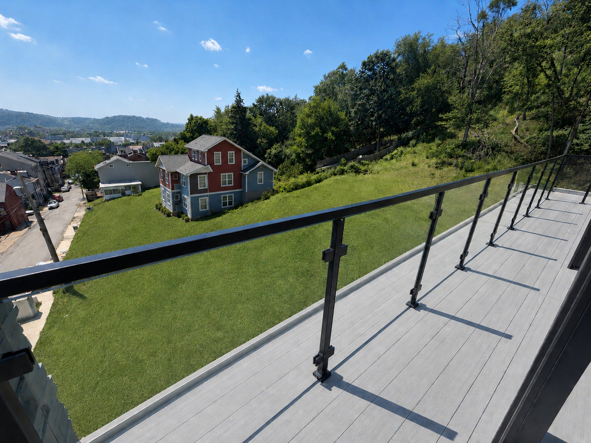 Modern black glass railing overlooking a renovated blue and red house on a green hillside in Pittsburgh